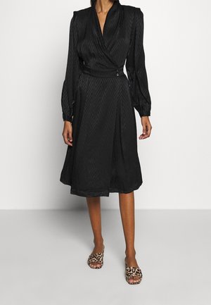 Black wrap dress with a chevron pattern, long puff sleeves, and a belt at the waist. Paired with leopard print slide sandals.