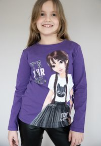 T-shirt a maniche lunghe viola con una grafica di una ragazza con treccine, che indossa una maglietta con stampa di gatti, con il testo "È IL TUO GIORNO" in bianco e nero.