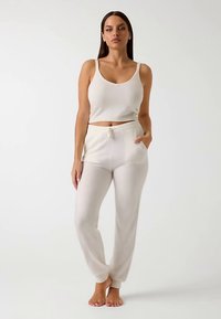 Ensemble lounge en maille crème claire comprenant un débardeur court et un pantalon à coupe décontractée avec taille à cordon de serrage et poches latérales.