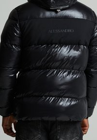 Schwarze Pufferjacke mit glänzender Oberfläche, die ein mattes Panel mit dem "ALESSANDRO"-Logo aufweist. Gestylt mit horizontalen gesteppten Segmenten.