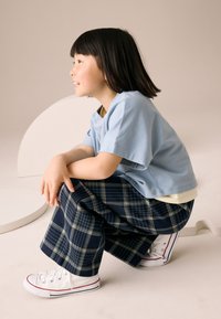 T-shirt azzurro chiaro a maniche corte, pantaloni a gamba larga a quadri blu navy e sneakers bianche con dettagli rossi. Materiale morbido in cotone, vestibilità comoda.