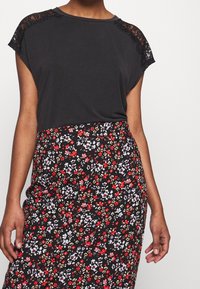 Svart kortärmad topp med spetstillägg vid axlarna, i kombination med en svart blommig pennkjol med röda, vita och blå blommor.