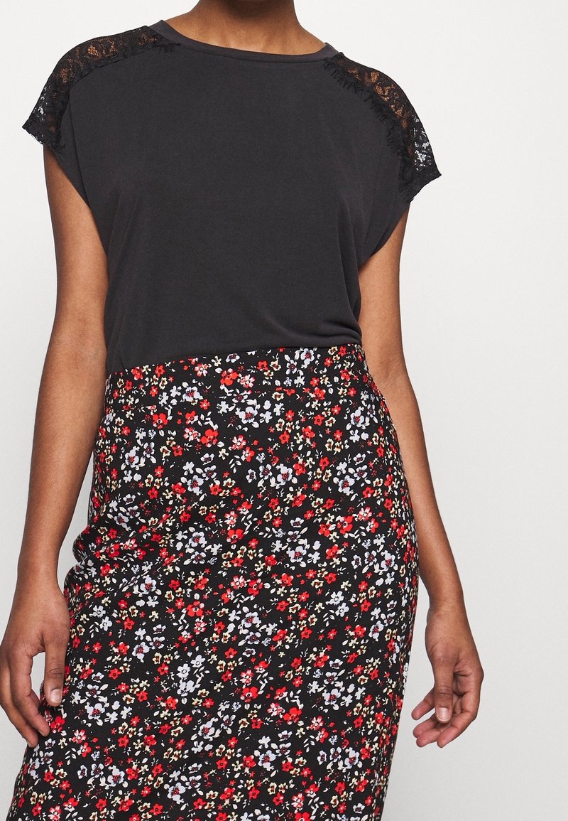 Svart kortärmad topp med spetstillägg vid axlarna, i kombination med en svart blommig pennkjol med röda, vita och blå blommor.