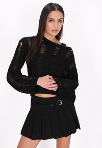 Schwarzer, kurzer Pullover mit strukturiertem, offenem Strickdesign und weiten Ärmeln, kombiniert mit einem strukturierten, schwarzen Plisseerock mit Gürtel.