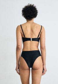 Črni bikini set, ki vključuje bandeau zgornji del z nastavljivimi tankimi naramnicami in zlatim zaključkom, v kombinaciji z visokim pasom.