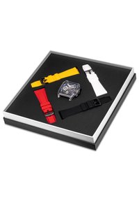 Horloge met heldere kast en zwarte wijzerplaat, vergezeld van vier siliconen horlogebanden in rood, geel, wit en zwart, tentoongesteld in een doos.