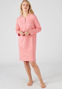 Abito da notte a maniche lunghe in cotone rosa chiaro. Presenta un'apertura con bottoni, una tasca con motivo a pois e spacchi laterali.
