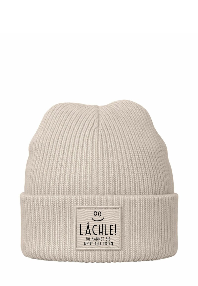 Light beige knitted beanie with a ribbed texture and folded cuff. Features a rectangular label with black text and a smiley face detail.