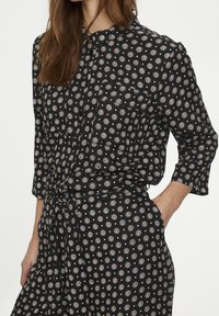 Robe noire à motifs avec un imprimé rond en blanc et orange, devant boutonné, manches trois-quarts et détail de taille nouée.