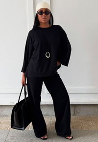 Svart lös sittande topp och vida byxor med en slät textur. Accessoarer med ett långt svart halsband och en strukturerad svart handväska.