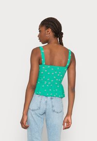 Top peplum floral verde com alças largas e um design de costas quadradas, feito de um tecido leve, combinado com jeans azul-claro de cintura alta.