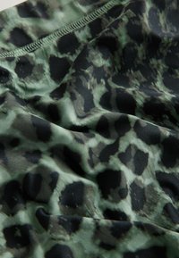 Leoparda raksta audums zaļu un melnu toņu krāsās, ar gludu faktūru, spīdīgu virsmu un izsmalcinātu raksta detaļu.