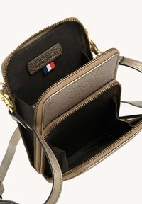 Sac de travers en métal doré compact avec deux compartiments zippés, intérieur en tissu noir et une petite étiquette en tissu rouge, blanc et bleu à l'intérieur.