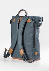 Roll-Rucksack aus weichem, dunkelblauem Leder mit braunen Lederelementen; verfügt über gepolsterte Träger und eine seitliche Reißverschlusstasche.