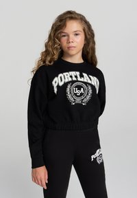 Felpa nera con la scritta "PORTLAND" e "USA" stampata in bianco. Presenta una vita elasticizzata e polsini. Abbinata a leggings neri con logo.