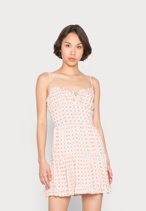 Sundress com padrão floral em rosa claro, com bainha com babados, alças de espaguete ajustáveis e um corpete justo com detalhe de laço na frente.