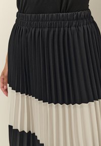 Skládaná sukně s černým pasem, střídajícími se černými a krémovými panely se vzorem cikcak, vyrobená z hladké, texturované látky.