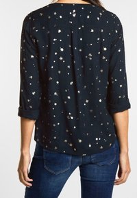 Marinblus med metalliska guldprickar, med rundad halsringning och uppvikta ärmar. Slät tyg med avslappnad passform.