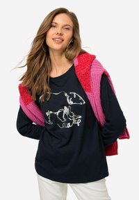 Czarna koszula z długim rękawem z srebnym graficznym motywem zwierzęcym. W zestawie z dzianinowym różowo-czerwonym szalem, noszonym na białych spodniach.