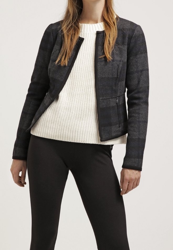 Giacca a quadri nera con un design aderente e una texture morbida, abbinata a un maglione in maglia crema. Leggings neri completano l'outfit.
