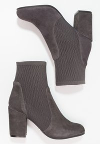 Szare botki na kostkę z teksturowaną górną częścią z dzianiny i gładkimi akcentami z zamszu, z masywnym obcasem dla stabilności. Minimalistyczny design.