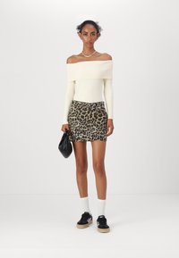 Béžový rebrovaný sveter bez ramienok, skombinovaný s mini sukňou so leopardím vzorom. Modelka drží čiernu tašku a má na sebe čierne tenisky s bielymi ponožkami.