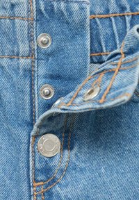 Svetlomodrá denim textília so striebornými kovovými cvokmi a kontrastným oranžovým prešívaním. Obsahuje preložený klapku s viditeľnými detailami prešívania.