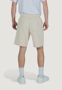 Pantaloni corti beige con vita elastica, tessuto morbido, design fino al ginocchio, abbinati a calze bianche e sneaker. Vista posteriore mostrata.
