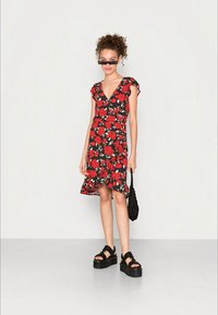 Vestuário preto com flores e rosas vermelhas, mangas curtas com babados e barra rodada. Combinado com sandálias de plataforma pretas e uma bolsa texturizada preta.