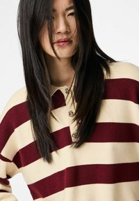 Poliestera polo krekls ar svītrainu rakstu bēša un vīna krāsā, ar apkakli un dekoratīvām pogām. Audumam ir mīksta tekstūra un brīvs piegriezums.