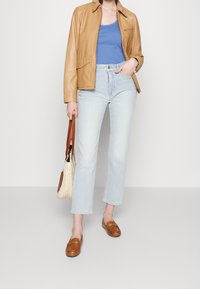 Brun läderjacka, blå linne, ljusblå croppade jeans, bruna loafers och en vävd väska. Fokus på struktur och avslappnade designinslag.