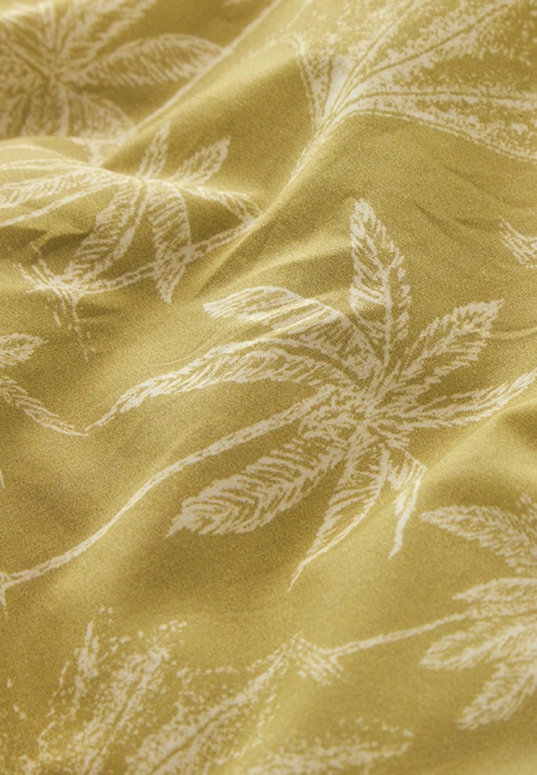 Tissu à base vert olive avec un motif de feuilles de palmier blanches, présentant une texture douce et un design légèrement froissé.