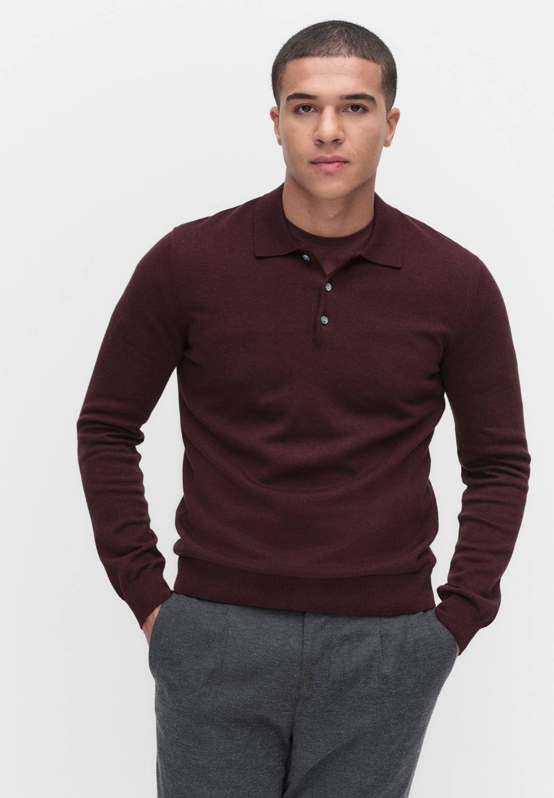 Burgundy pitkähihaisen polo-neuleen, jossa on ribbetty helma ja kaulus, varustettuna kolmella napilla ja sileällä pinnalla. Yhdistetty harmaisiin housuihin.