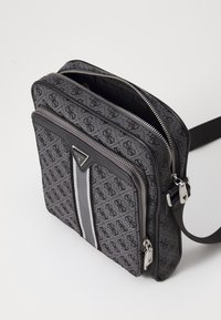 Bolso cuadrado gris con un patrón texturizado y rayas grises. Presenta doble cremallera, un acento de cuero negro y una correa ajustable.