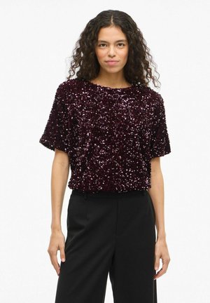 Bordeaux kleurige sequin top met korte mouwen, ronde halslijn en een ontspannen pasvorm. Gecombineerd met zwarte, op maat gemaakte broeken voor contrast.