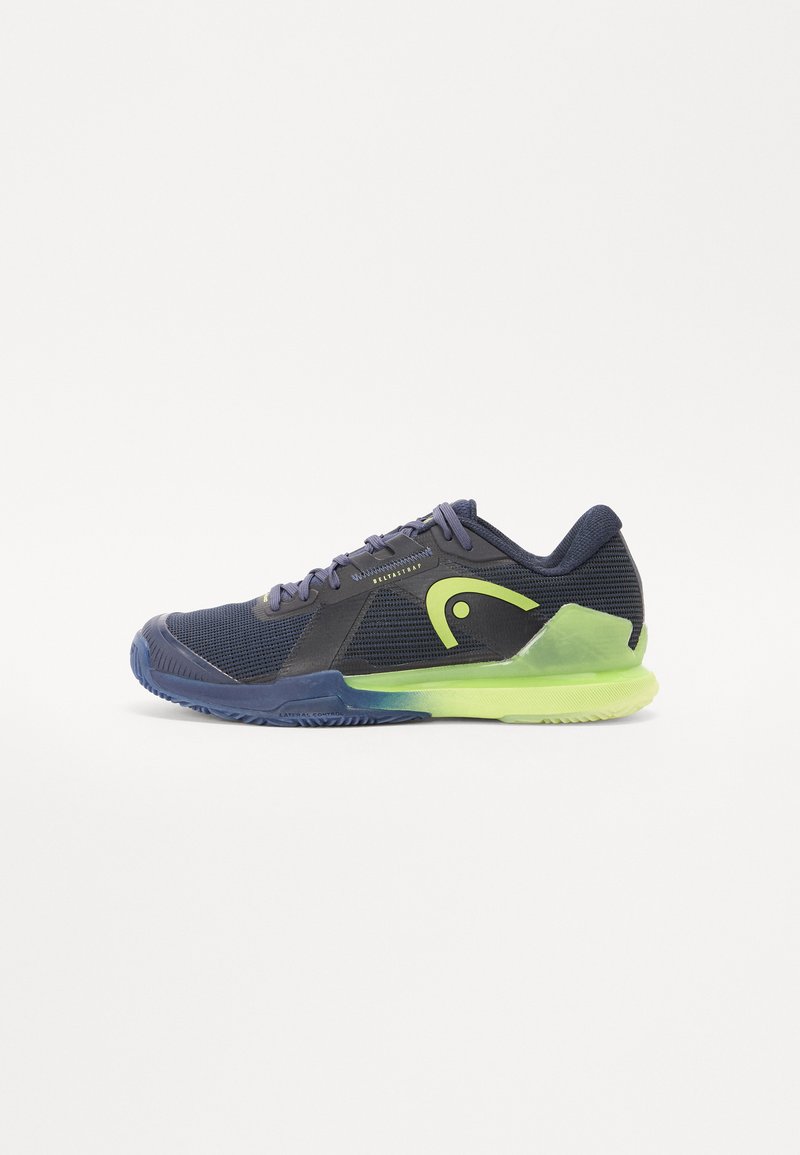 Navy athletic shoe with mesh upper, green accents, textured black overlays, and a blue rubber sole. Features a low profile design and laces.