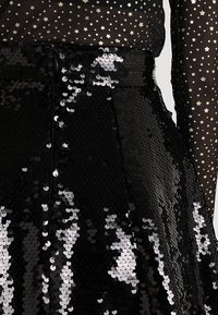 Falda negra con lentejuelas que presenta un diseño acampanado y lentejuelas brillantes, combinada con una blusa negra transparente con patrones de estrellas doradas.