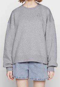 Šedá mikina s kulatým výstřihem, spadlými rameny a ribbovanými manžetami. Na hrudi se nachází malé černé logo Jordan. Nosit over denimovými šortkami.