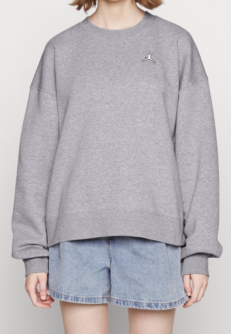 Šedá mikina s kulatým výstřihem, spadlými rameny a ribbovanými manžetami. Na hrudi se nachází malé černé logo Jordan. Nosit over denimovými šortkami.