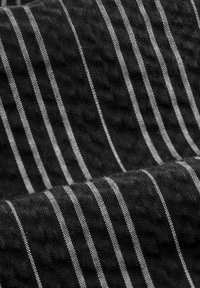 Svart texturerad tyg med vita vertikala ränder. Texturen verkar vävd med ett lätt dimensionellt mönster genom hela.