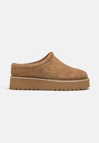 Scarpa slip-on in suede marrone con punta rotonda, suola piatta a profilo basso e dettagli di cucitura lungo il lato. Finitura texturizzata e liscia.