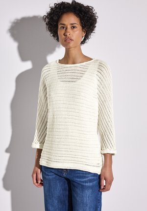 Maglione di colore crema chiaro in maglia, con strisce orizzontali, scollo a barca e maniche a tre quarti. Abbinato a jeans di denim blu.