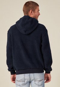 Sweat à capuche en polaire bleu marine avec une surface texturée, doté d'une capuche, de poignets côtelés et d'une coupe décontractée. L'arrière est uni, sans embellissements.