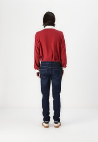 Rød genser med rund hals, paret med mørkeblå denimjeans. Teksturiert stoff og tettsittende design. Hvit kragedetalj synlig.
