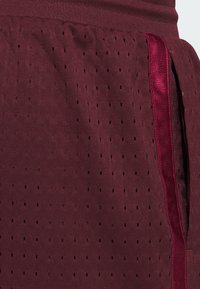 Maroon athletic shorts with a perforated texture, elastic waistband, and a contrasting dark red side stripe. Features side pockets.