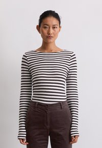 Langsleeve gestreepte top in wit en bruin met een bootnek. Gecombineerd met donkerbruine corduroy broek. De stof ziet er glad en aansluitend uit.