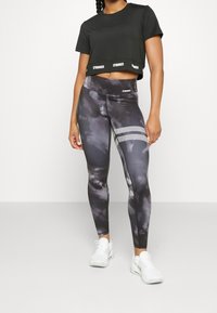 Camiseta negra recortada con el logo "STRONGER" en el dobladillo, combinada con leggings de tie-dye en gris y negro que cuentan con rayas de malla y un diseño ajustado.