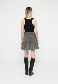 Črn brezrokavnik v kombinaciji s kovinsko srebrno krilom s flared krojem, črne čizme do kolen, prikazano s hrbtne strani na belem ozadju.