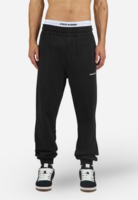 Black sweatpants with elastic waistband and cuffs, featuring a white "PEGADOR" logo on the left thigh. Made from soft, smooth fabric.