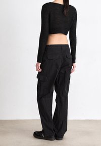 Suéter negro recortado con mangas largas, tejido texturizado, combinado con pantalones cargo negros que cuentan con bolsillos laterales y traseros.